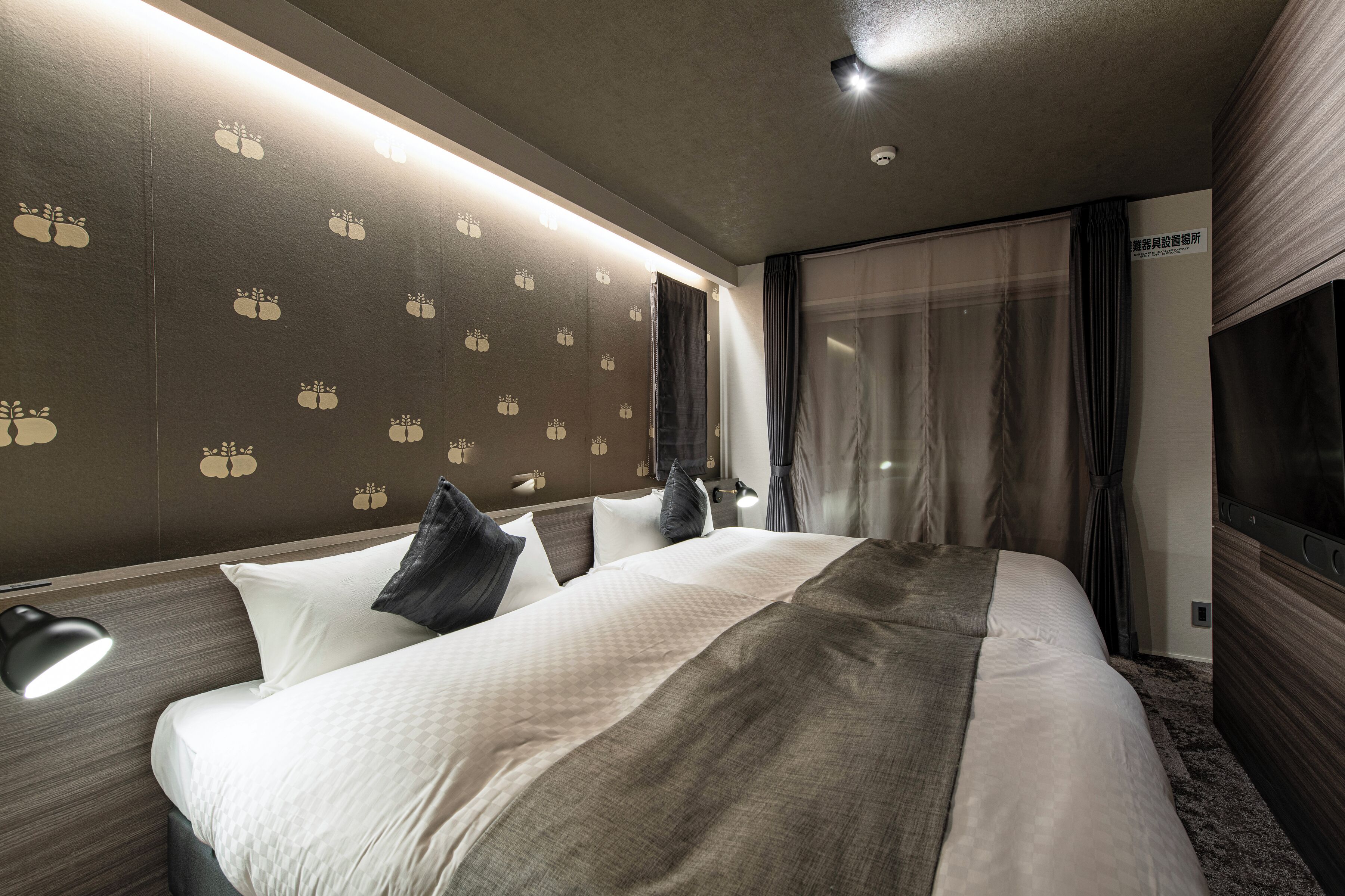 A modern hotel room with a large bed, a bedside lamp, and a wall with a pattern of tree designs.