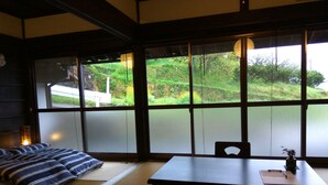 A traditional Japanese room with tatami flooring, a low table, and a sofa with striped cushions. - Kumano Kodo Nagano Guesthouse (Tanabe)