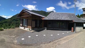 A traditional Japanese building with a sloped tiled roof, wooden exterior, and a gravel driveway with white circular markers. - Kumano Kodo Nagano Guesthouse (Tanabe)