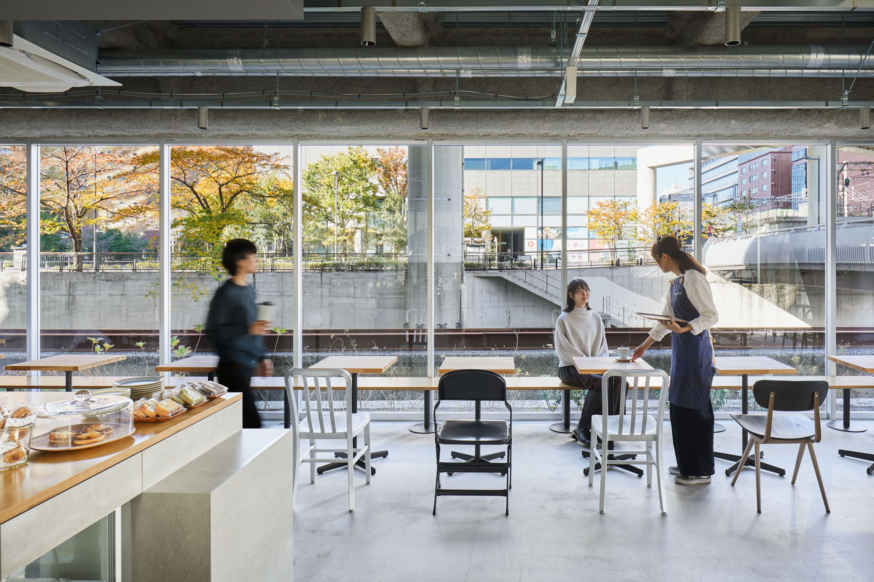 An indoor space with large windows, a counter with food items, and several tables and chairs.