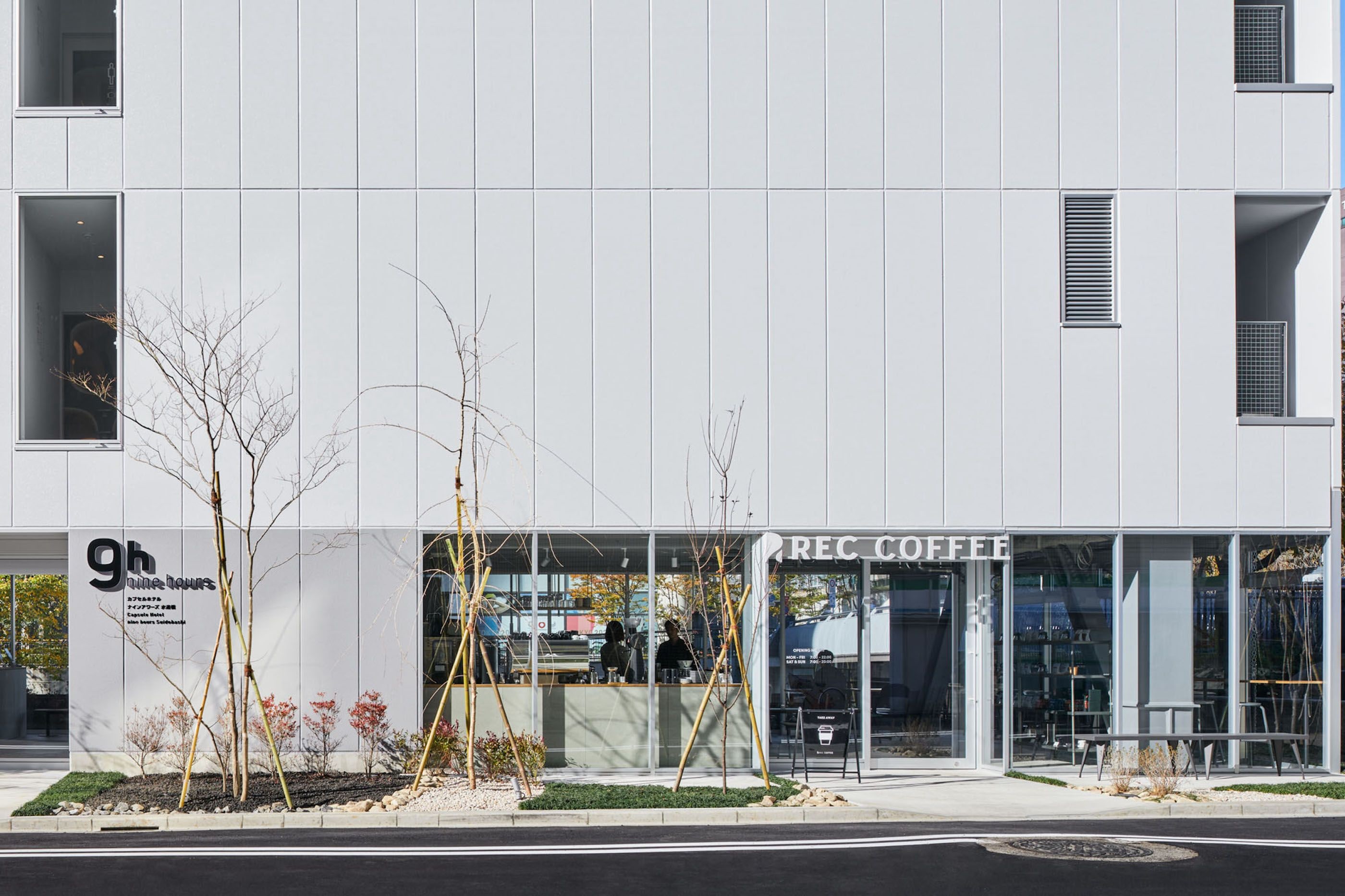 Um edifício moderno com fachada de vidro, um letreiro para o café '9h online hours' e o estabelecimento 'REC COFFEE'.