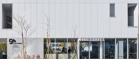 Um edifício moderno com fachada de vidro, um letreiro para o café '9h online hours' e o estabelecimento 'REC COFFEE'.