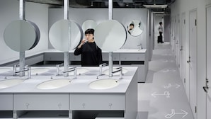 Un baño moderno con varios lavamanos, espejos y flechas en el suelo indicando la dirección.