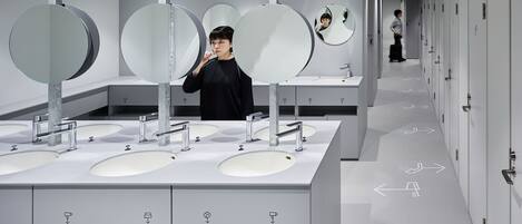 Un baño moderno con varios lavamanos, espejos y flechas en el suelo indicando la dirección.