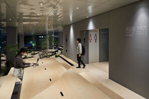 A modern interior with a glass wall, a seating area with tables, and an elevator with gender-specific signage.