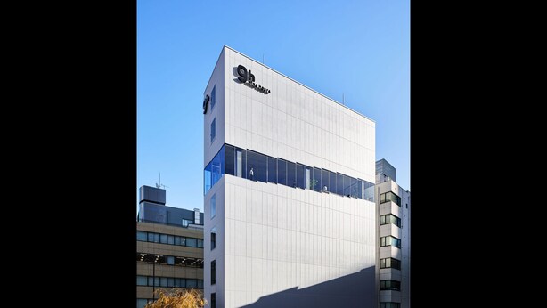 Un edificio moderno con un llamativo letrero '9h', grandes ventanales y techo plano.