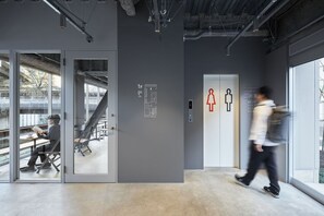 An interior space with a staircase leading to a lower level, a glass door entrance, and a wall with directional signs. - 9h nine hours Suidobashi (Tokyo)