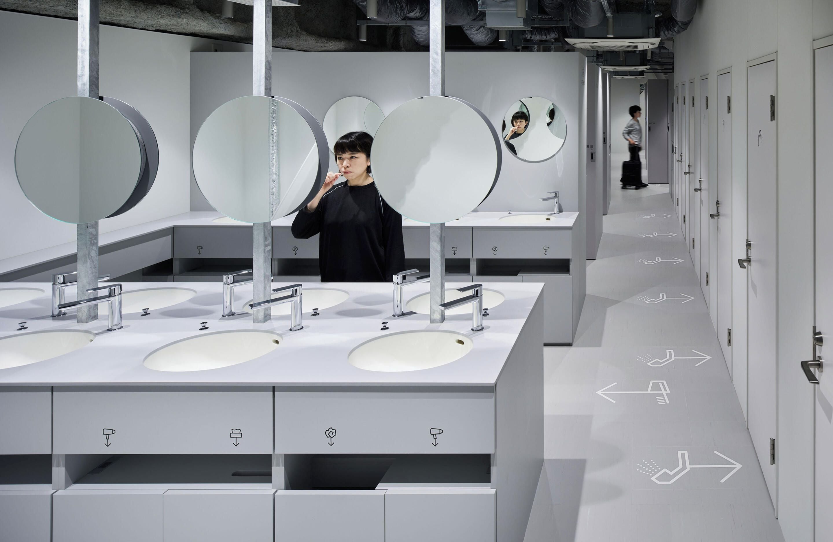 A modern bathroom with multiple sinks, mirrors, and directional arrows on the floor.