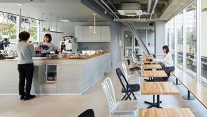 Un café moderno con una barra alargada, zona de estar y grandes ventanales.