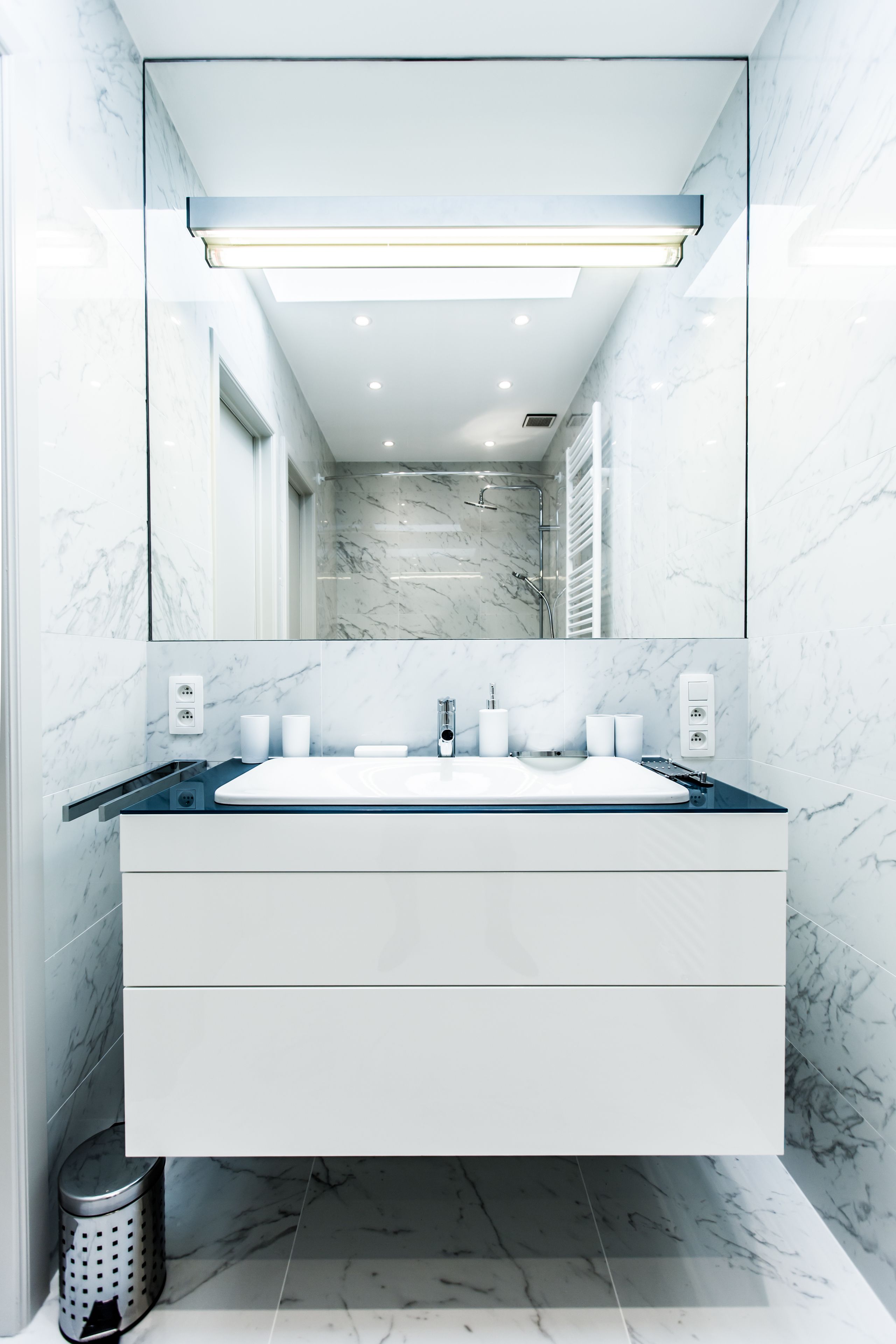 A modern bathroom with a large mirror, white marble tiles, a white sink, and a blue countertop.
