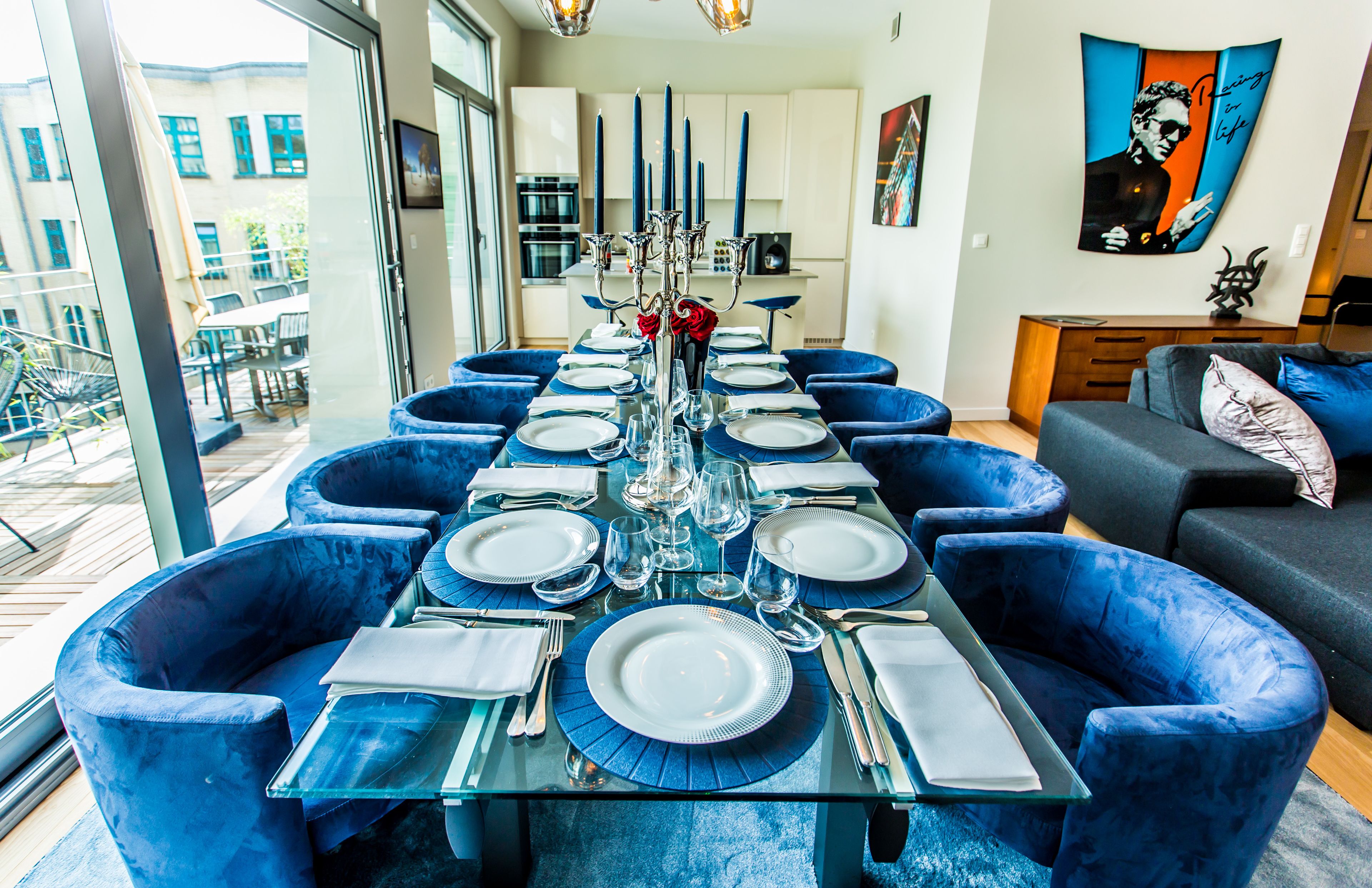 Comedor con una mesa de vidrio dispuesta para seis personas, rodeado de sillas tapizadas en azul.