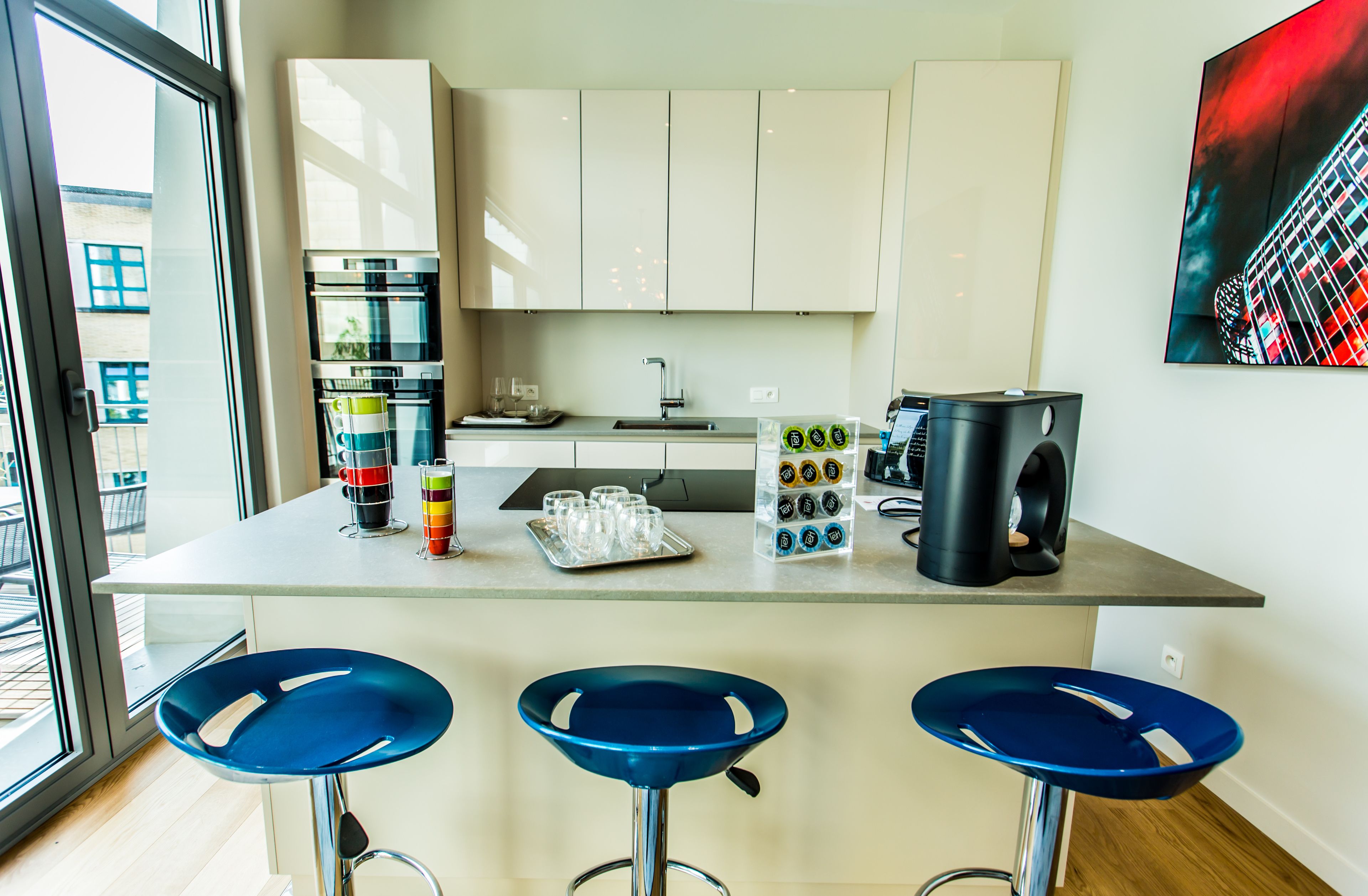 Una cocina moderna con una isla central, taburetes de bar, una cafetera y un ventanal grande.