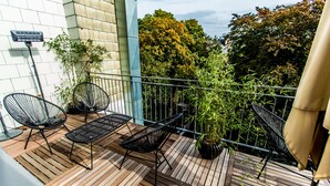 A wooden deck with two black metal chairs and a table, surrounded by potted plants and a metal railing.
