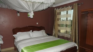 A single bed with a wooden headboard, white bedding, and a green accent. - Omega Gardens Hotel (Karatina)