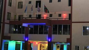 The Omega Gardens Hotel with multiple floors, a prominent sign, and flags on the roof. - Omega Gardens Hotel (Karatina)