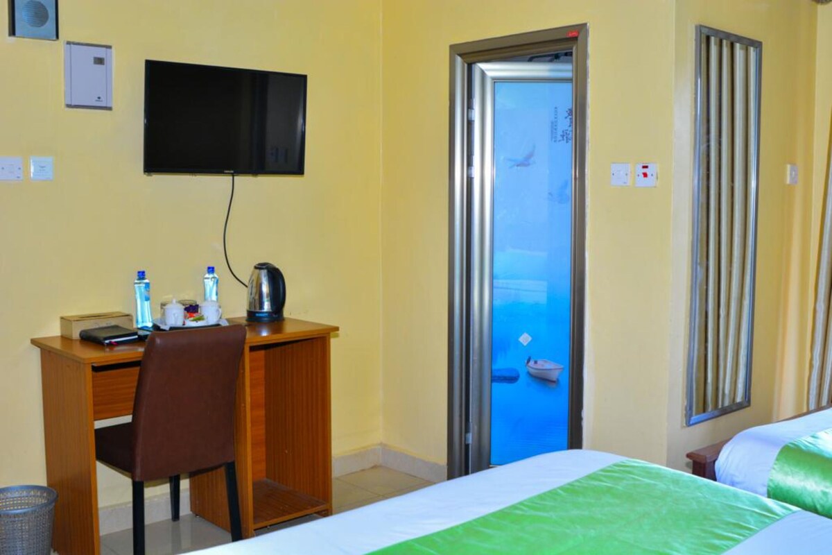 A hotel room with a bed, a desk with a chair, a television, and a door leading to a balcony.