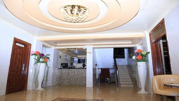 A reception area with a reception desk, a staircase, and a chandelier. - Omega Gardens Hotel (Karatina)
