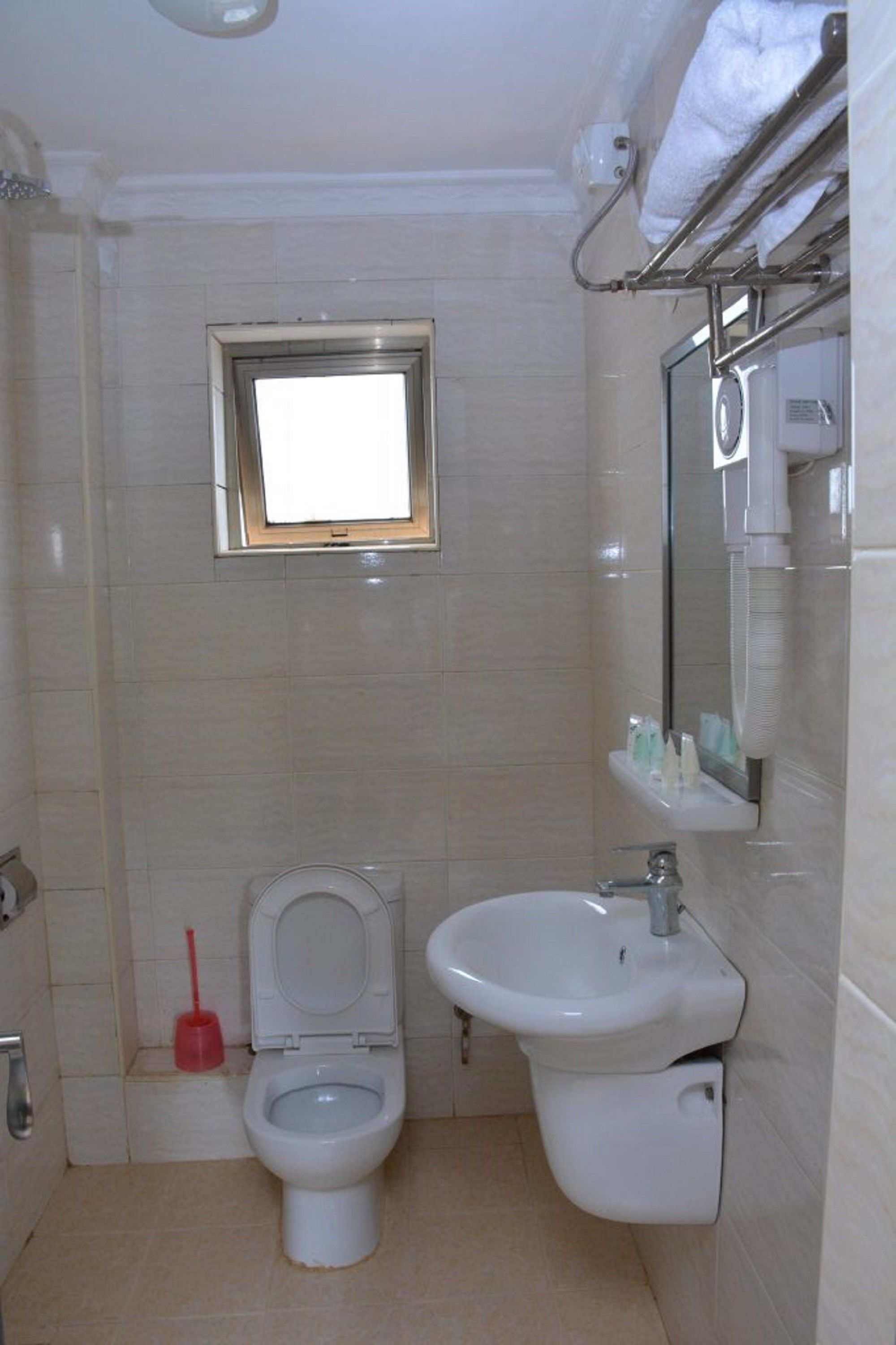 A small bathroom with a toilet, sink, and a window above the toilet.