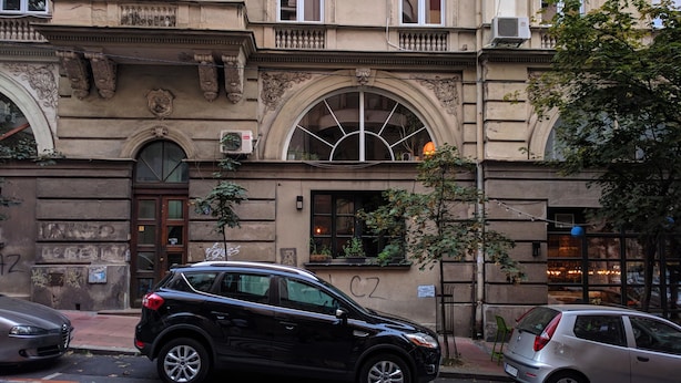 A black SUV parked on a street with a building featuring arched windows and a door with a window above it. - Basco Central Apartment Little Bay (Belgrade)