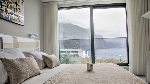A bedroom with a large bed, a view of the sea, and a mountain in the background. - Calamar Hotel (São Vicente)