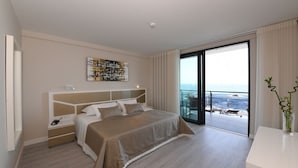 A modern hotel room with a large bed, a bedside table, a nightstand, a large window with a view of the sea, and a decorative plant. - Calamar Hotel (São Vicente)