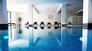 A swimming pool with clear blue water, surrounded by lounge chairs and a clock on the wall. - Calamar Hotel (São Vicente)