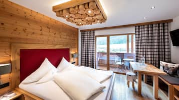 Ett hotellrum med en sänggavel i trä, en säng med vita sängkläder, ett matbord och en utsikt över ett snötäckt landskap genom fönstret.