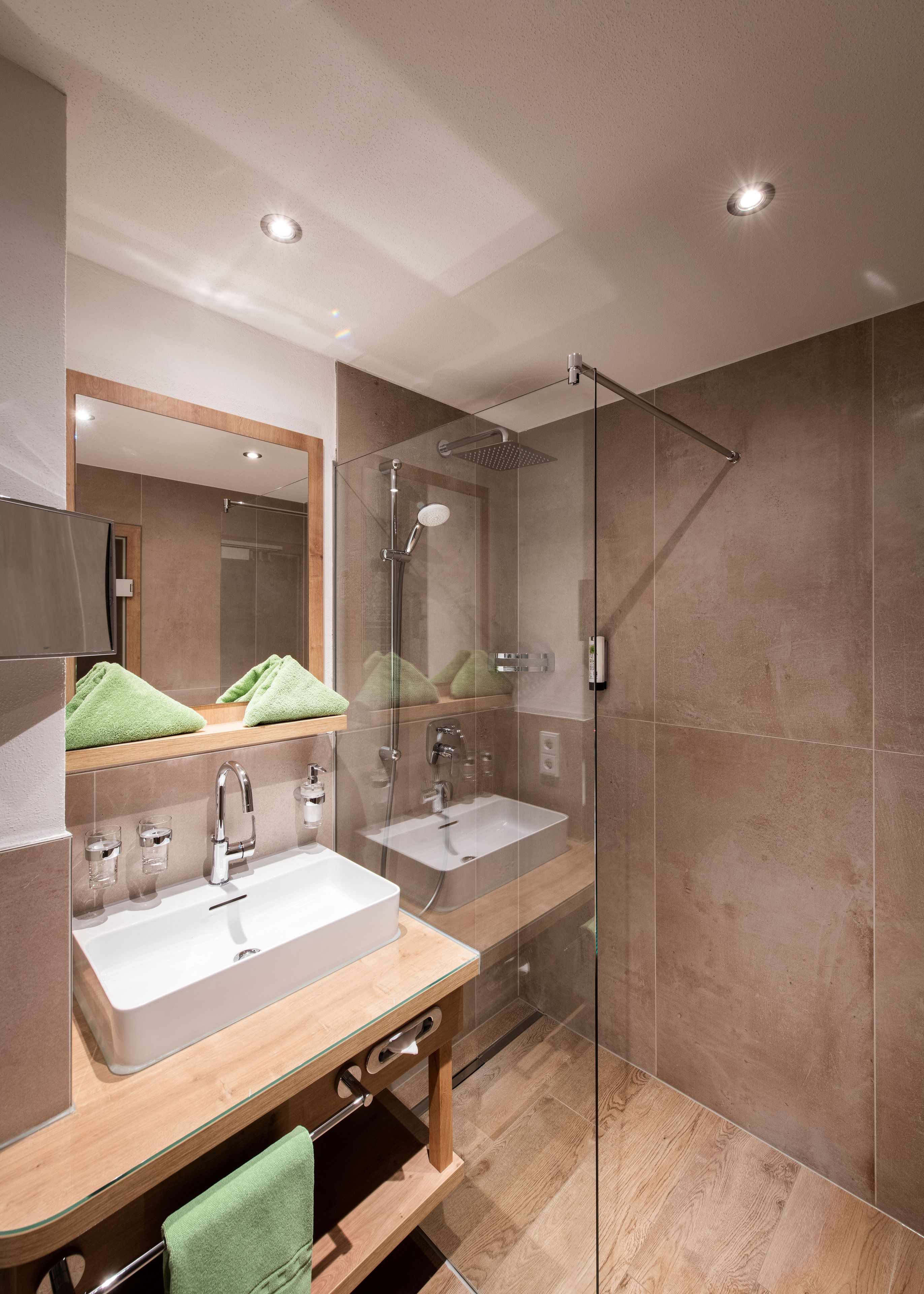 Un baño moderno con dos lavamanos, ducha con cerramiento de vidrio y un espejo grande.