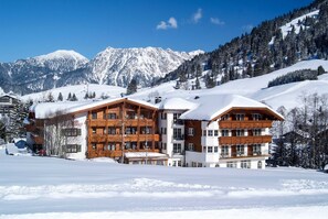 A multi-story wooden building with balconies, surrounded by snow-covered mountains and trees.