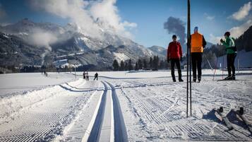 Ein verschneiter Skipisten mit Skifahrern, einem klaren Himmel und Bergen im Hintergrund.