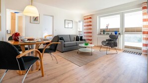 A modern living room with a sofa, dining table, chairs, and a balcony with a view.