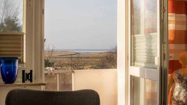 A room with a view of a field and a body of water.