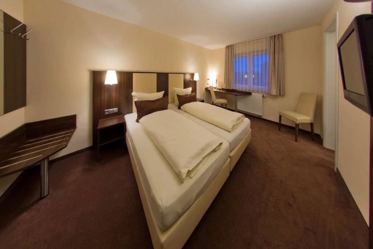 A hotel room with a double bed, a desk, a chair, and a TV.