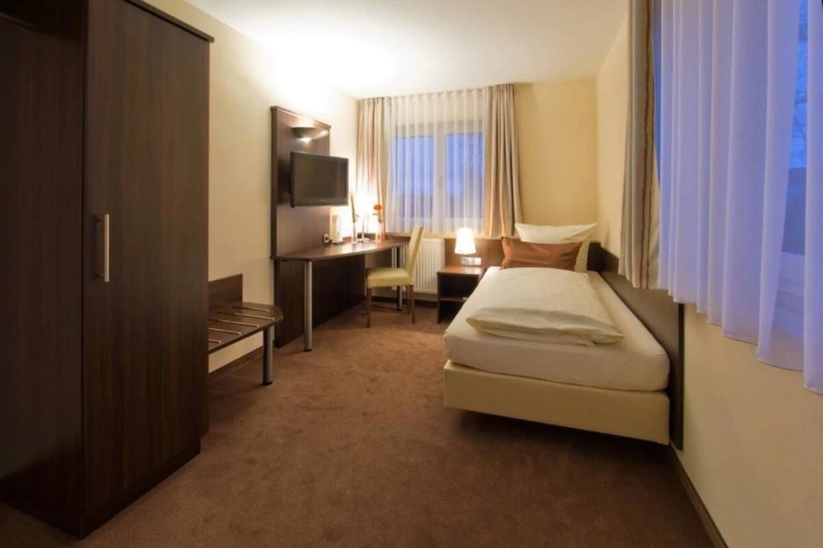 A hotel room with a bed, a desk, a chair, a television, and a wardrobe.