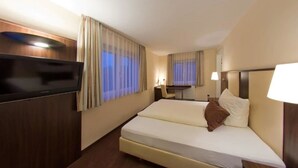 A hotel room with a bed, a desk, a television, and curtains. - Hotel-Restaurant Sonneneck (Dornstetten)