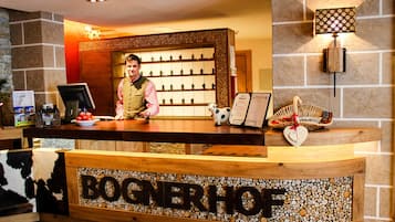 En receptionsdisk med en skylt som visar texten ”BOGNERHOF”, ett bord med ett urval av små figurer, en korg med ett hjärtformat föremål och en väggmonterad lampa.