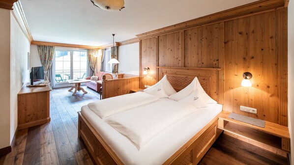 A hotel room with a large bed, wooden paneling, a desk with a computer, and a balcony with a view.