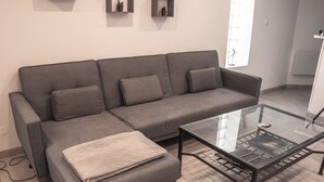 Un canapé d’angle gris avec un plaid, une table basse en verre et deux étagères murales ornées de petites plantes.