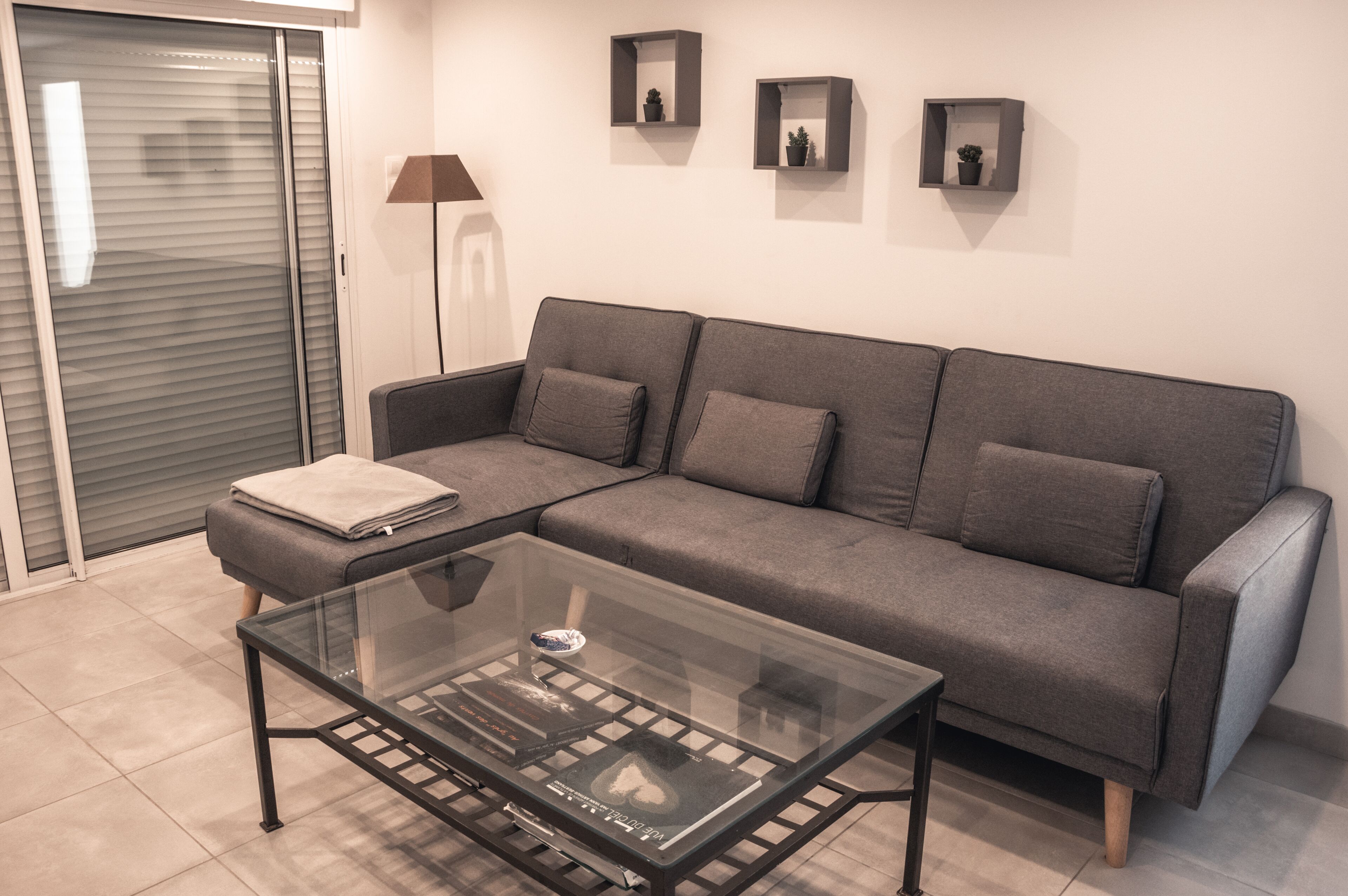 A modern living room with a grey sofa, a glass coffee table, and a closed sliding door.