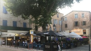 Un café en plein air, avec des tables et des chaises, entouré d’immeubles.