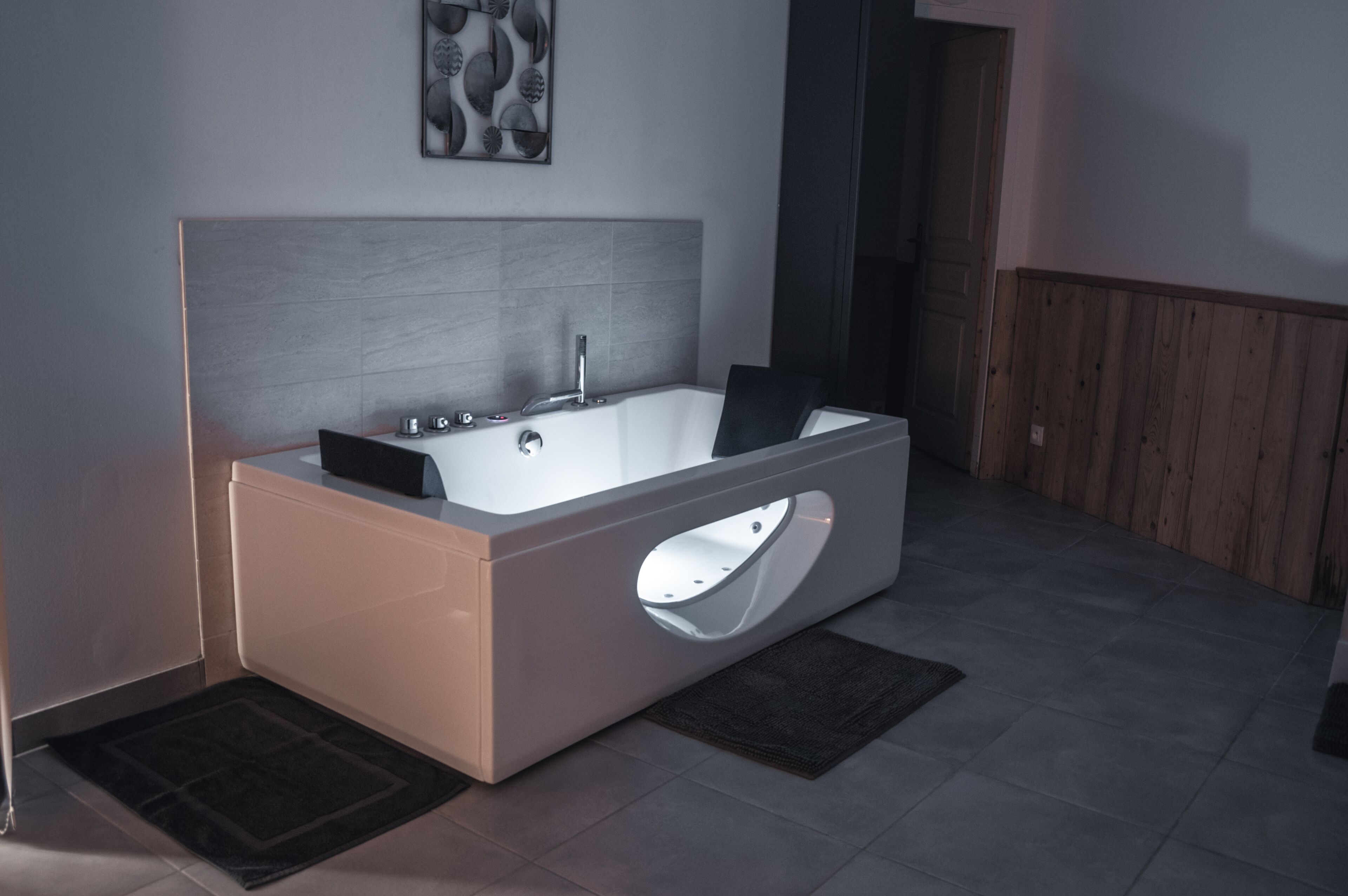 A modern bathroom with a large freestanding bathtub, a wall-mounted artwork, and a wooden panel wall.