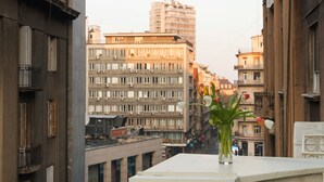 Une vue sur un paysage urbain avec de hauts immeubles, un ciel dégagé et un vase rempli de fleurs sur un balcon.