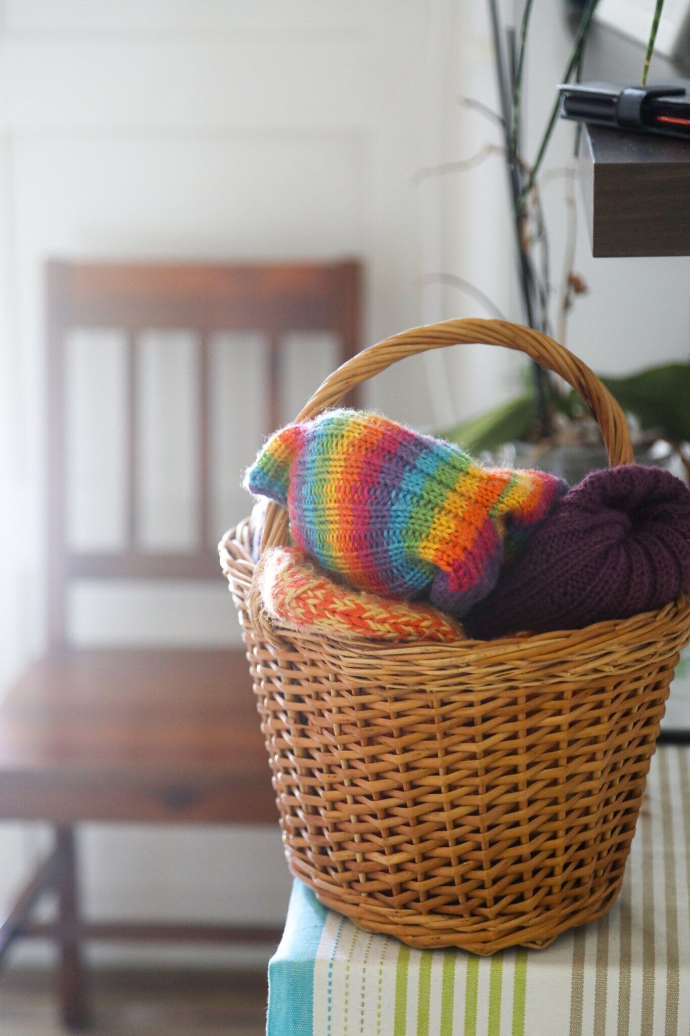 A wicker basket with colorful knitted items on a striped tablecloth.