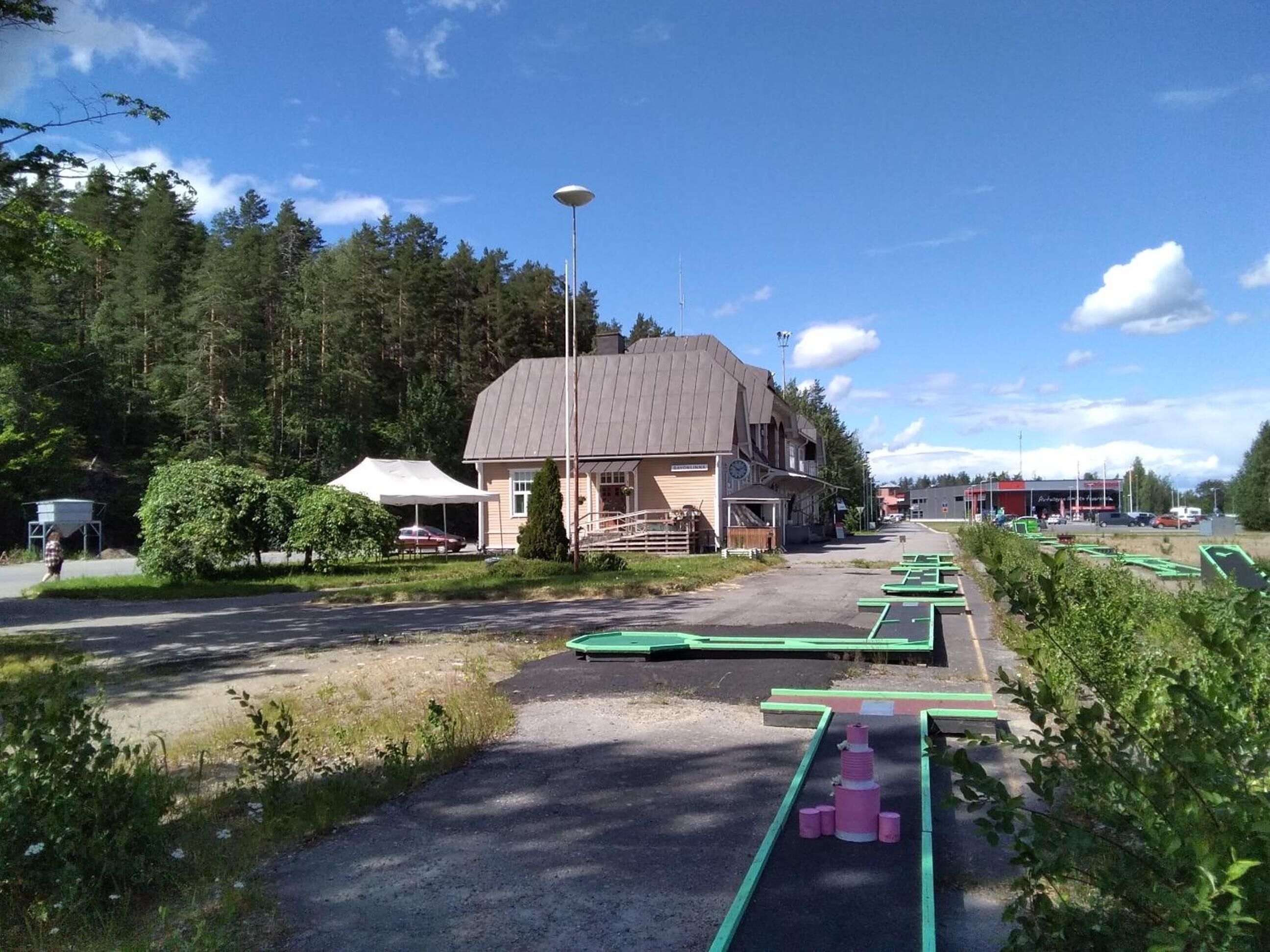 Un bâtiment doté d’un toit en pente, d’un espace extérieur couvert et d’un parking avec des tables de pique-nique vertes.