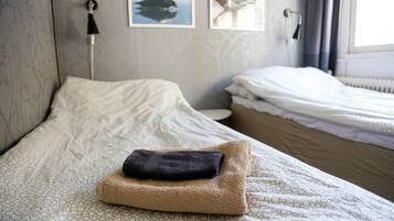 A neatly made bed with a folded towel and a pillow, a bedside table with a lamp, and a window with curtains.