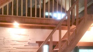 A wooden staircase with a metal railing leading to an upper level. Below, there is a television and a small table with a chair. - Rustic River Cabin under the Oaks and just a short walk to the river. (Uvalde)