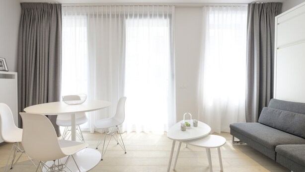 A modern living room with a grey sofa, a round dining table with white chairs, and a small side table. - White Studio (Brussels)
