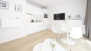 A modern kitchen with white cabinets, a dining area with white chairs, and a flat-screen TV mounted above the counter. - White Studio (Brussels)