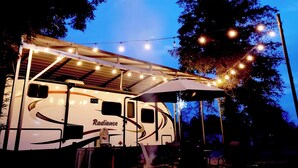 A RV named Radiance with a covered patio area, string lights, and a canopy.