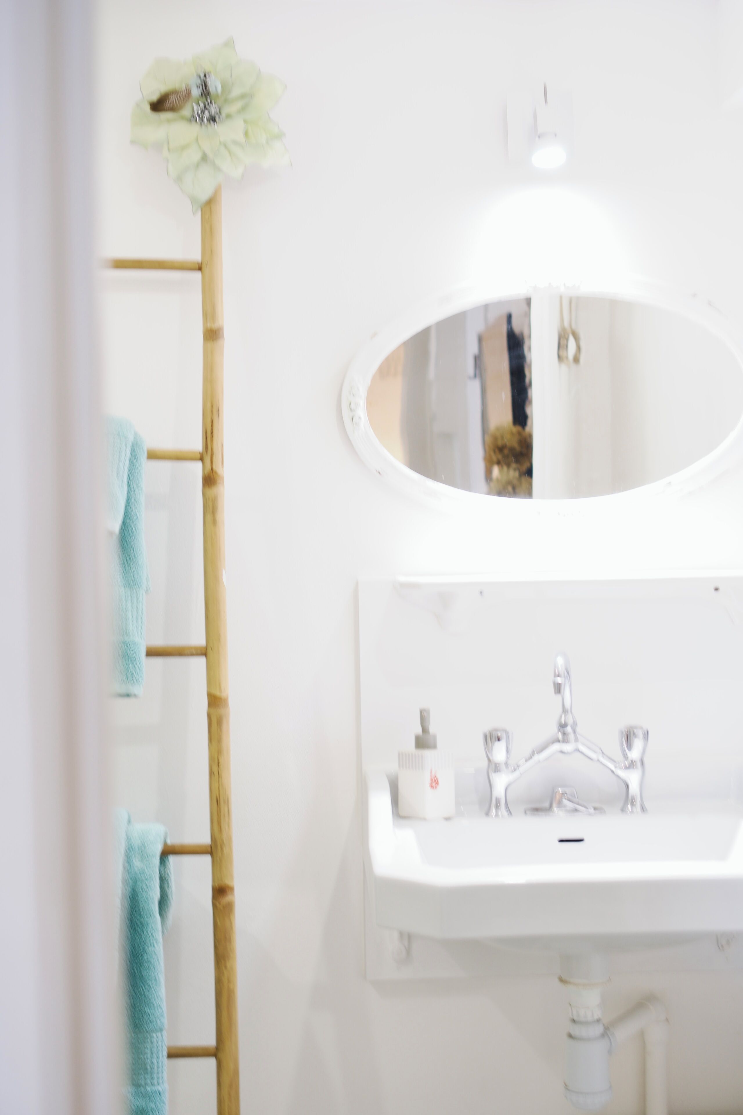 Un baño con un lavamanos blanco, espejo y un toallero con dos toallas.